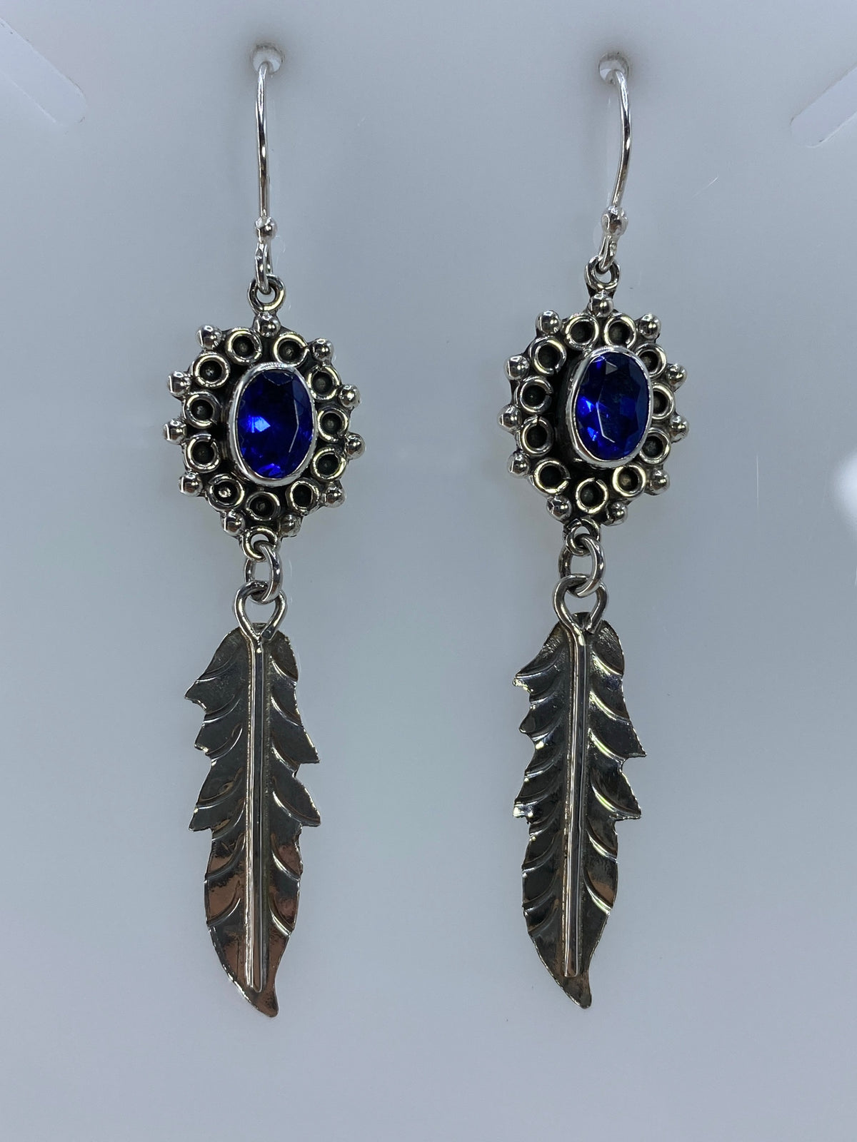 Detalle frontal de los aretes mostrando la circonia azul engastada y las plumas de plata