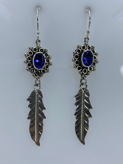 Detalle frontal de los aretes mostrando la circonia azul engastada y las plumas de plata