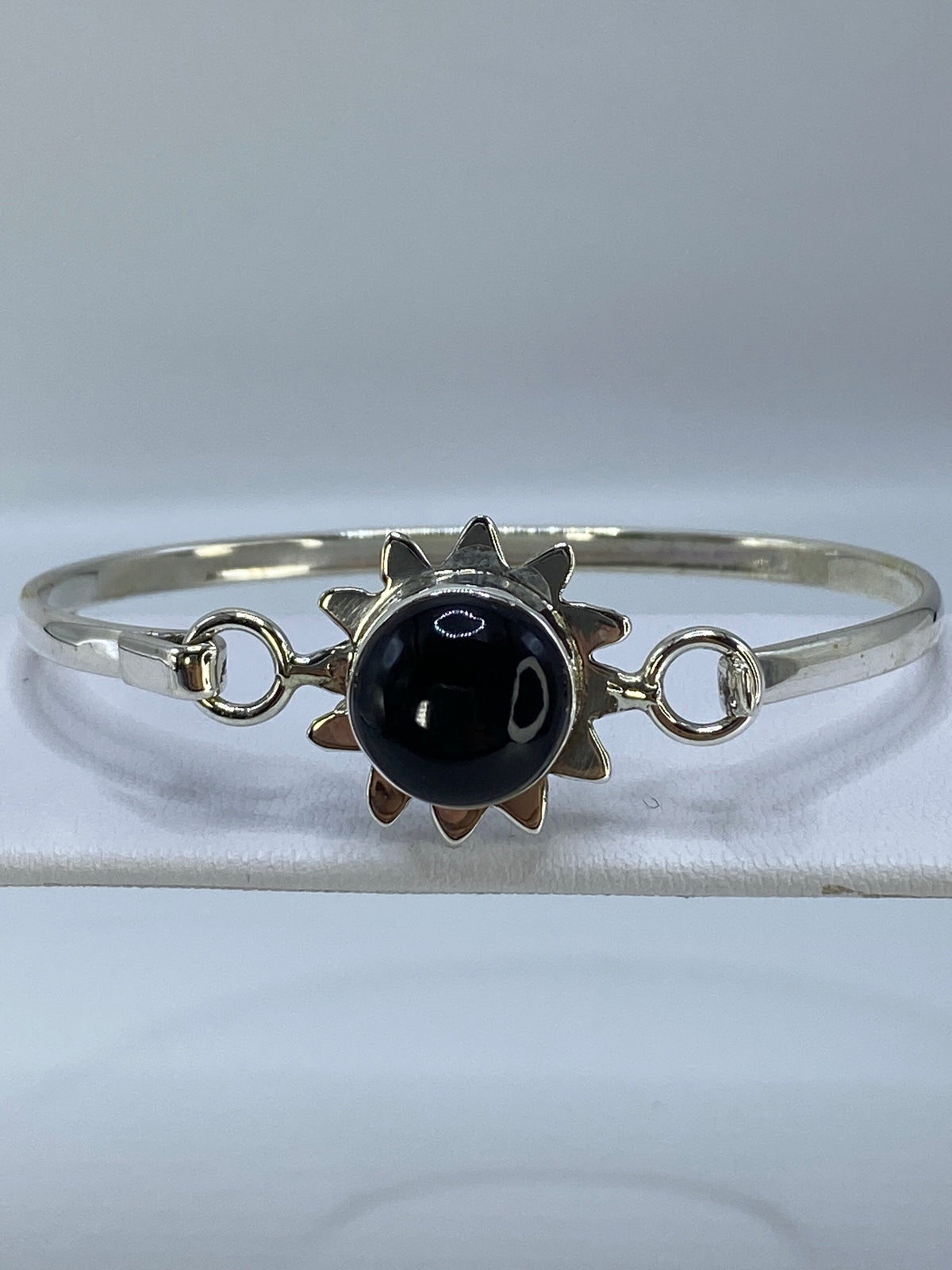 Brazalete rígido de plata con ónix negro engastado, visto de frente sobre fondo blanco
