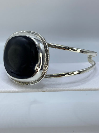Brazalete rígido de plata en ónix negro visto desde el lado, destacando el ancho de la banda