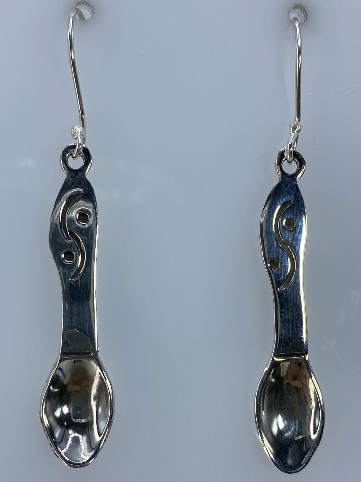 Aretes de plata con los ganchos extendidos en foto de escala con regla
