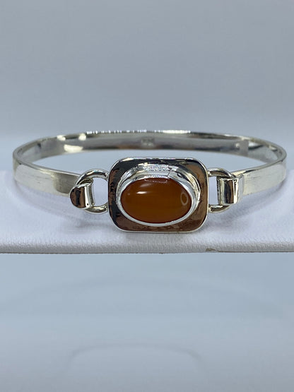 Brazalete de plata rígido con Ojo de Gato naranja en la muñeca de una mujer