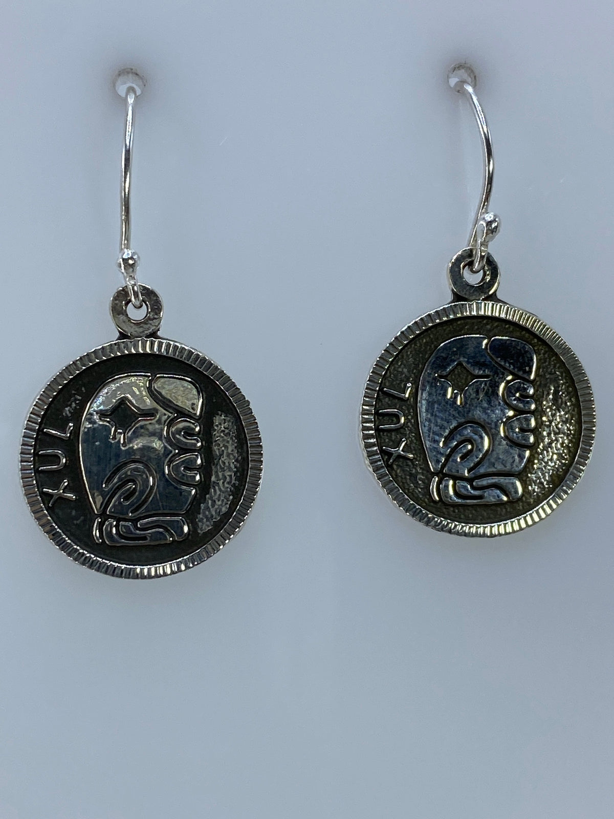 Par de aretes de plata con motivo prehispánico Xul repujado, en par colgando de ganchos de plata