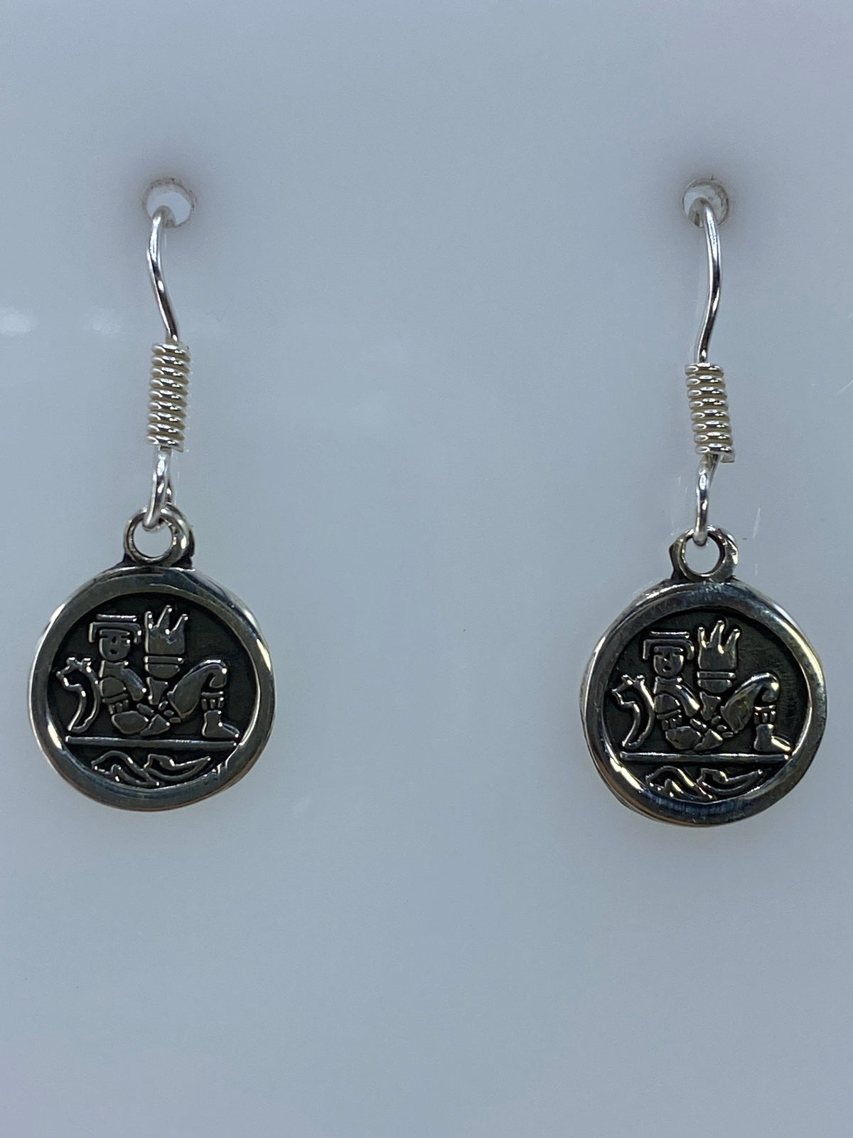 Par de aretes de plata con diseño prehispánico en relieve, colgando de ganchos de plata