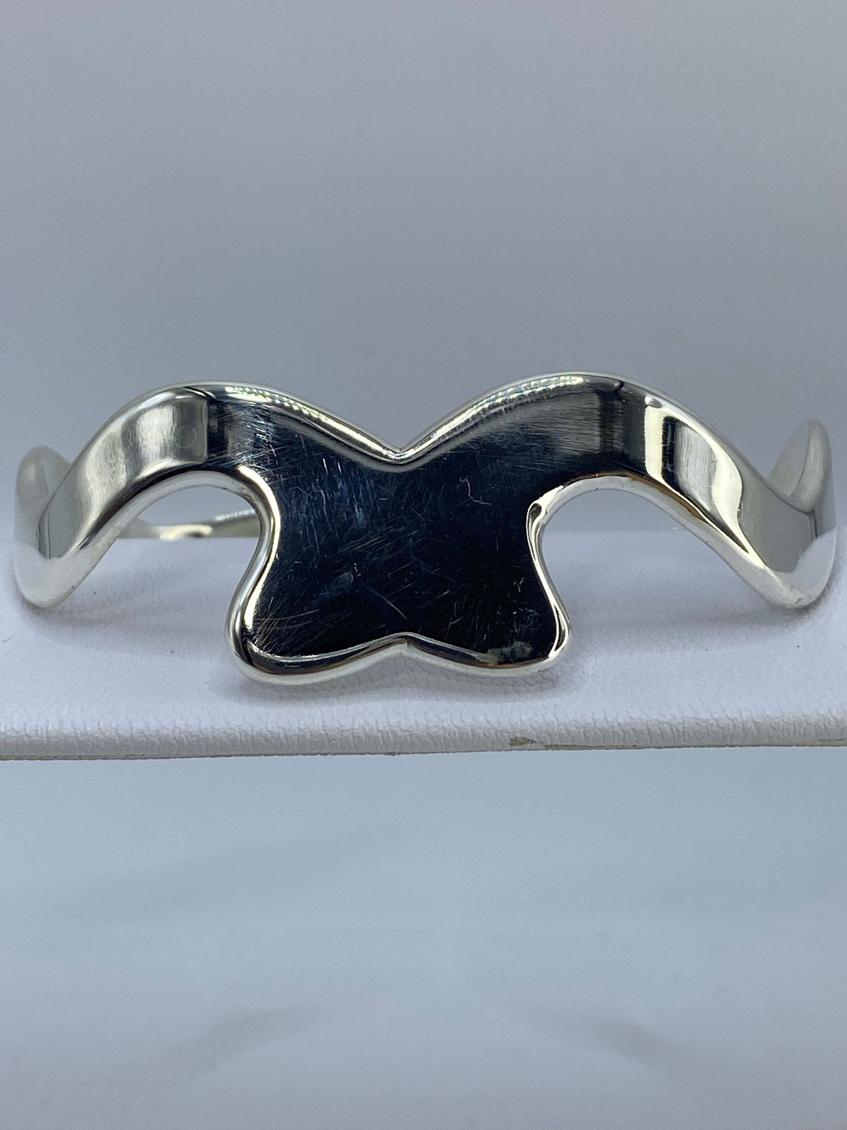 Brazalete rígido de plata cartoneado en la muñeca de una mujer, mostrando el volumen de la banda