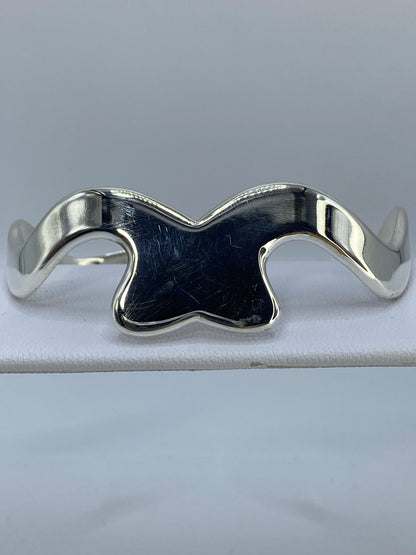 Brazalete rígido de plata cartoneado en la muñeca de una mujer, mostrando el volumen de la banda