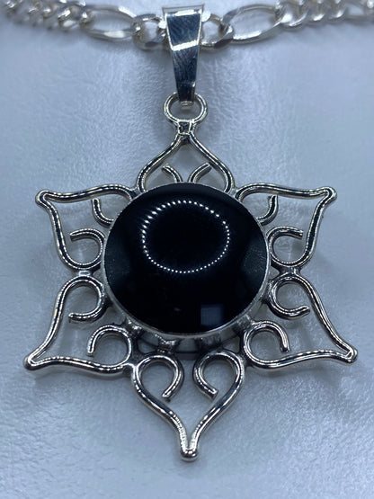 Vista frontal del dije mandala ónix negro 5.1 cm sobre cadena de eslabones plateados