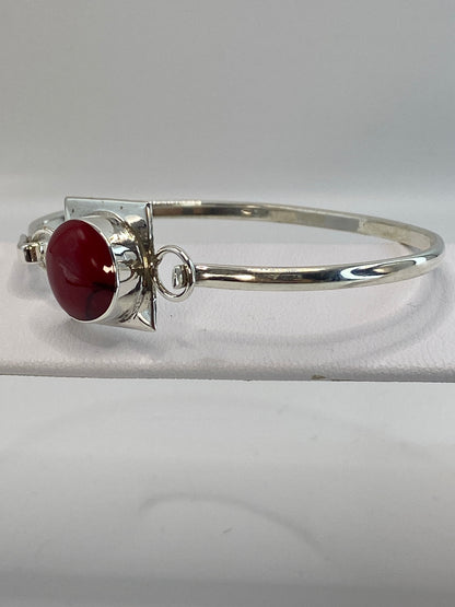 Brazalete rígido de plata con coral rojo sobre una mano, mostrando el diámetro interior