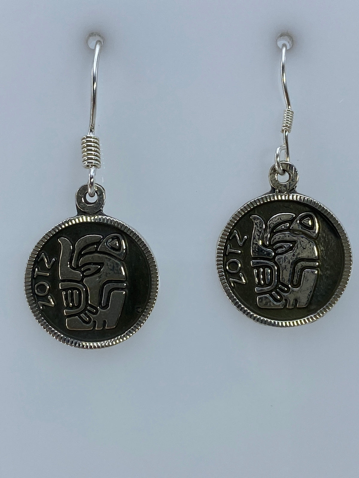 Par de aretes de plata repujado con motivo prehispánico azteca colgando