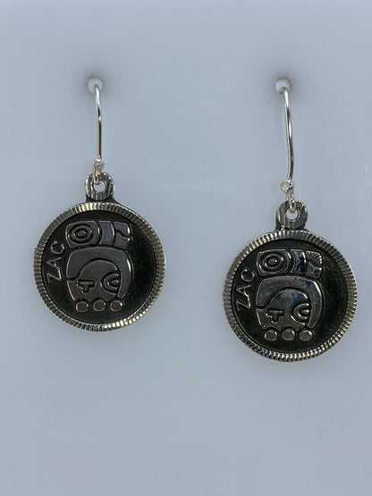 Par de aretes de plata repujado con motivo prehispánico de Taxco colgando del gancho