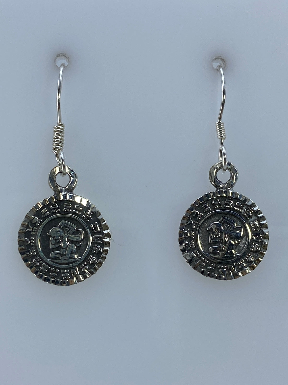 Par de aretes de plata 950 con repujado del Calendario Azteca colgando de gancho de plata