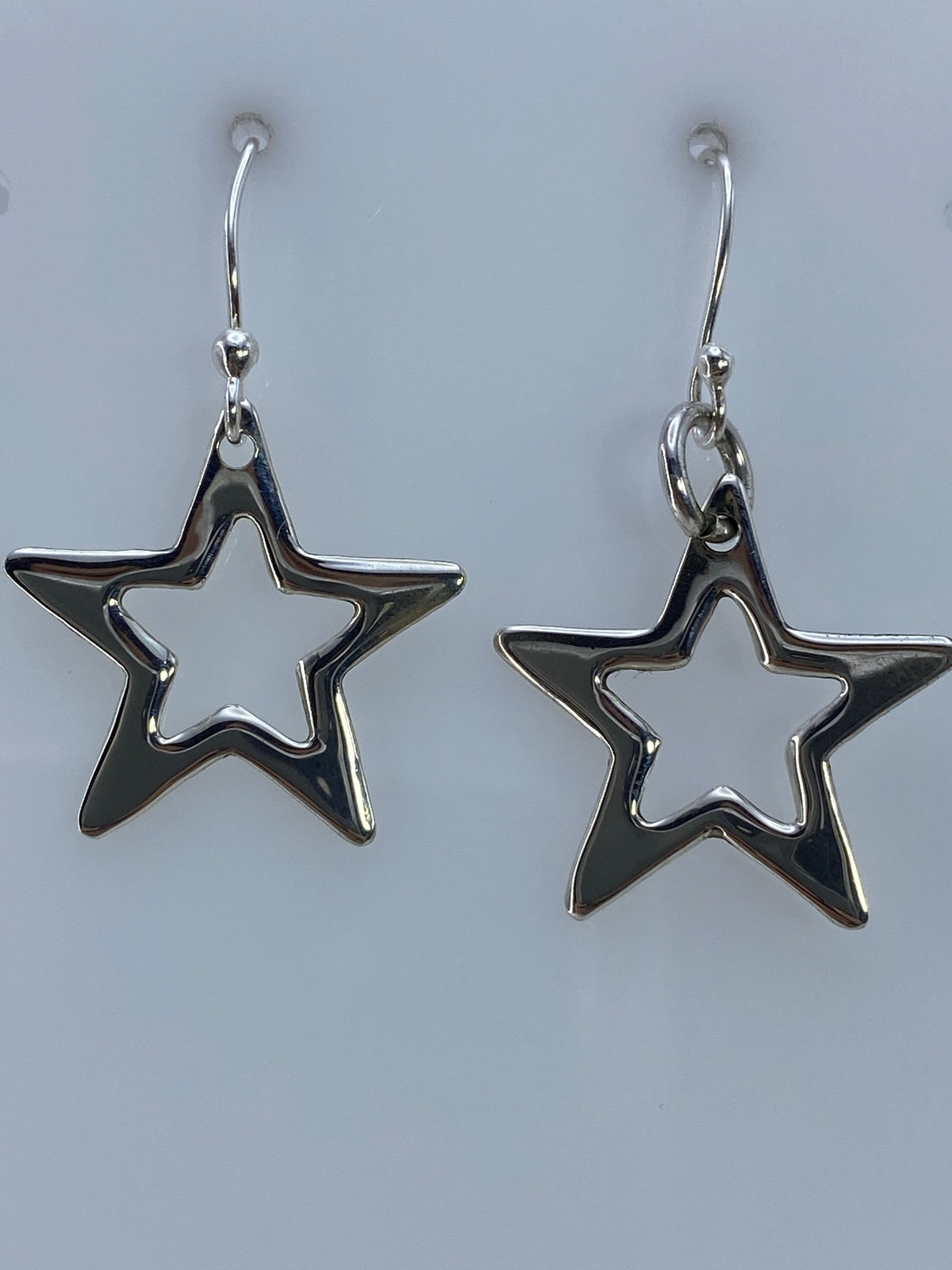 Par de aretes de plata con diseño de estrella calada, colgando del gancho