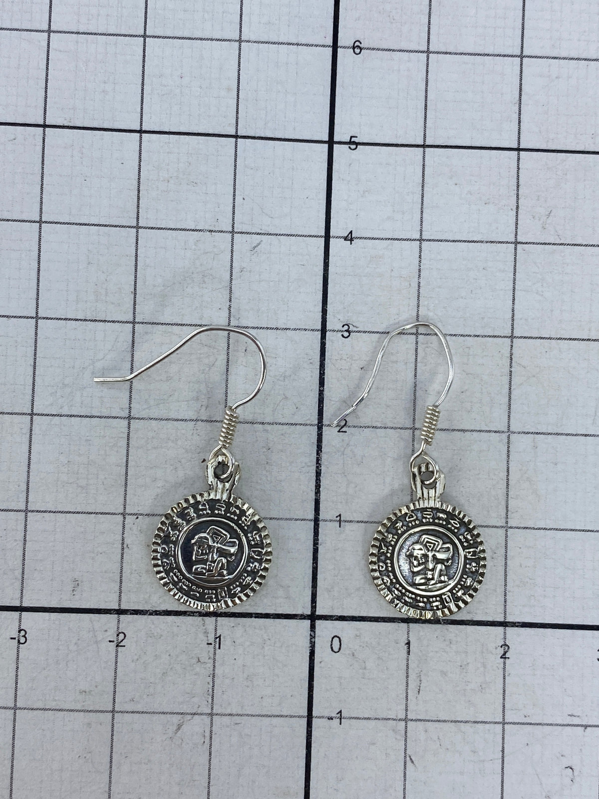 Pair of Taxco silver earrings with pre-Hispanic relief design on white background