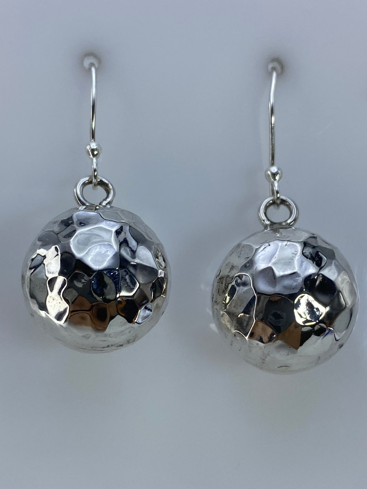 Par de aretes de plata cartoneado con diseño facetado, vistos de frente sobre fondo gris