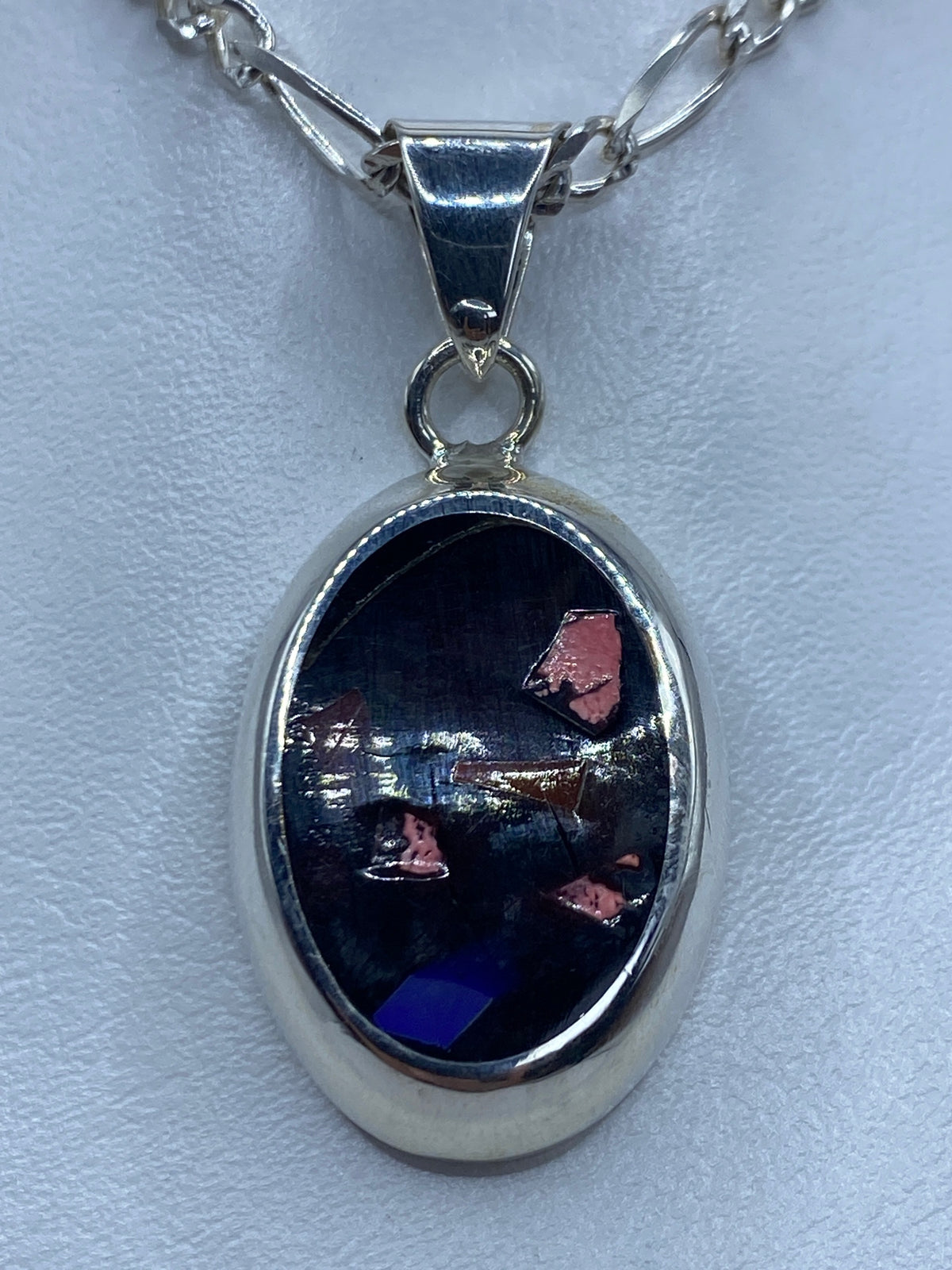 Dije ovalado de plata 925 con piedras multicolor engastadas, colgando de una cadena plateada