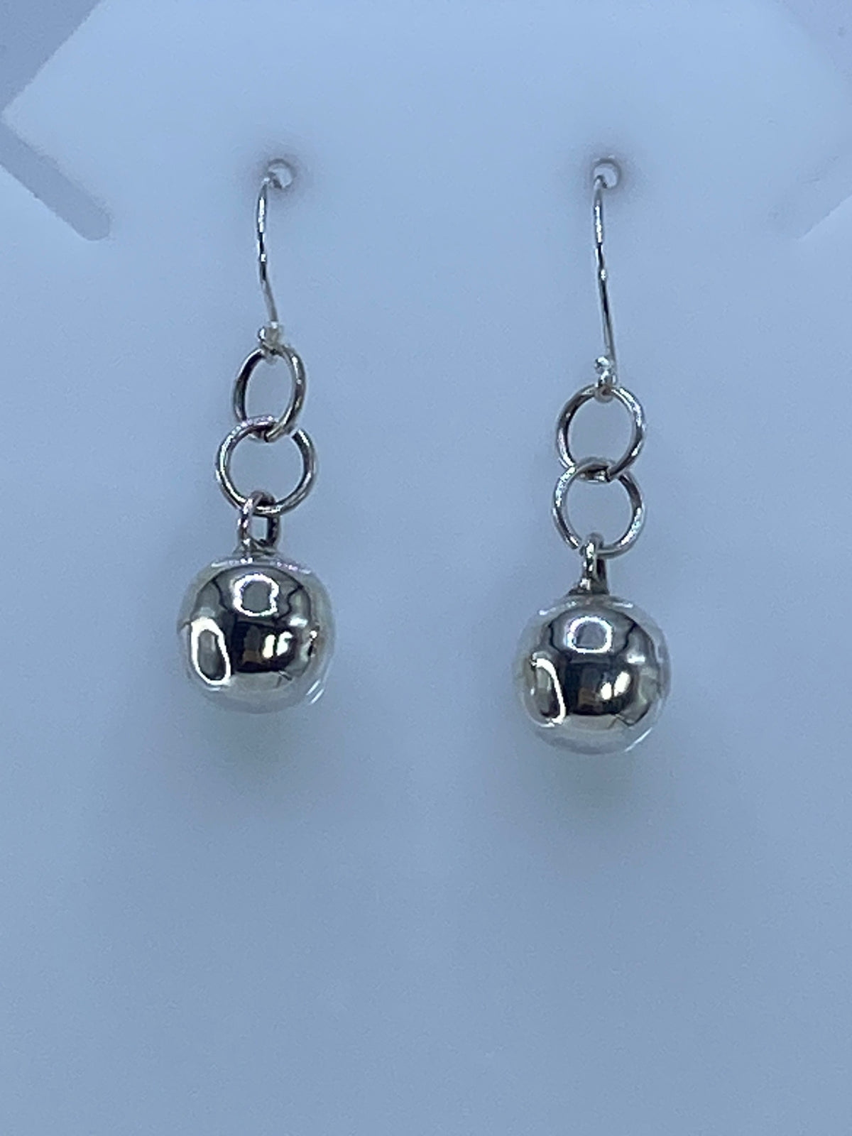 Par de aretes de plata con diseño geométrico cartoneado, colgando de ganchos