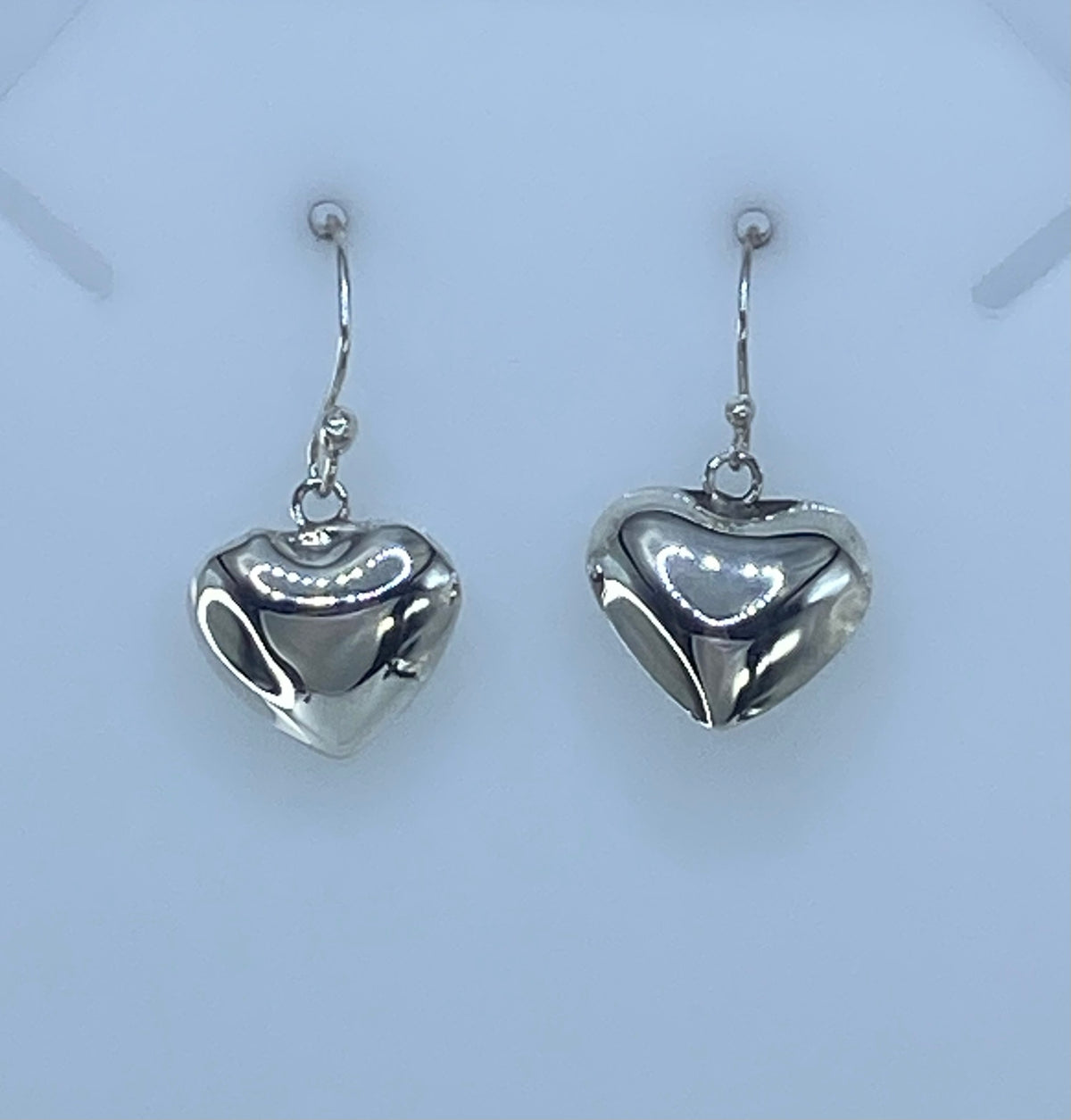 Aretes de plata corazón sobre fondo blanco, vista frontal de ambas piezas