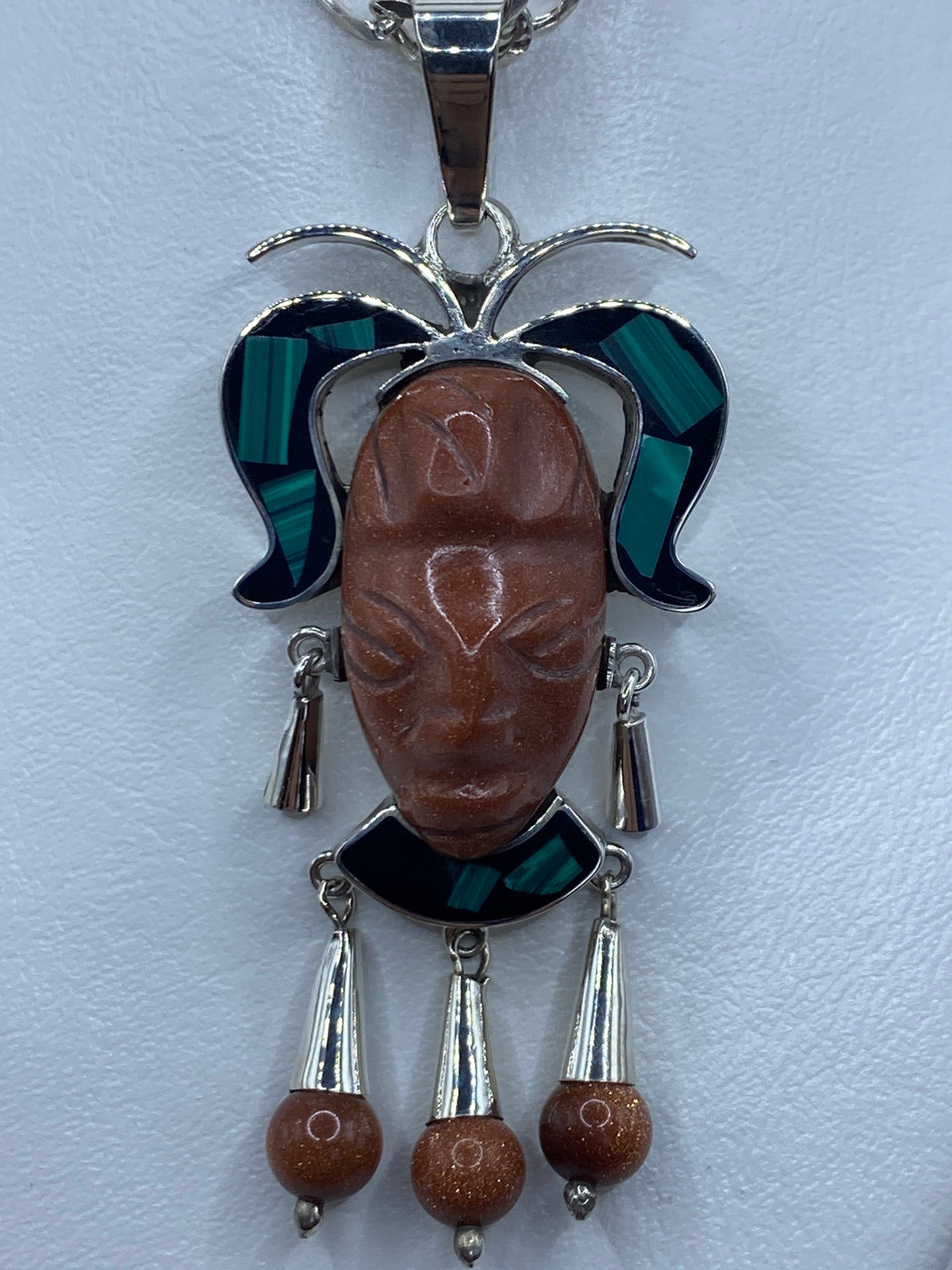 Detalle frontal del dije mostrando el repujado facial y las tres piedras combinadas