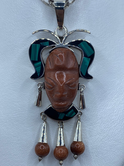 Detalle frontal del dije mostrando el repujado facial y las tres piedras combinadas