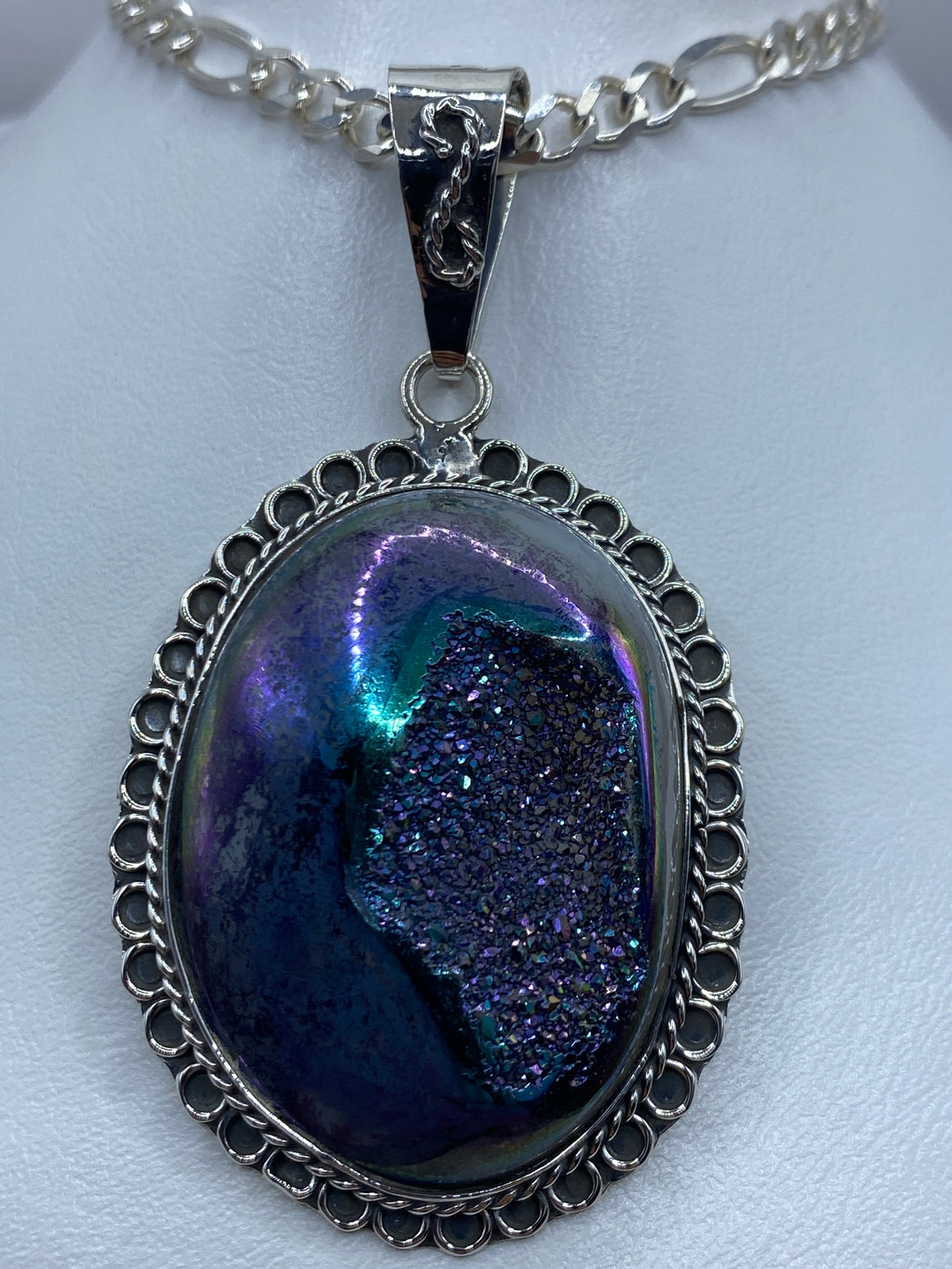 Dije ovalado de plata 925 con piedra morada engastada, marco calado de Taxco, colgando de cadena plateada