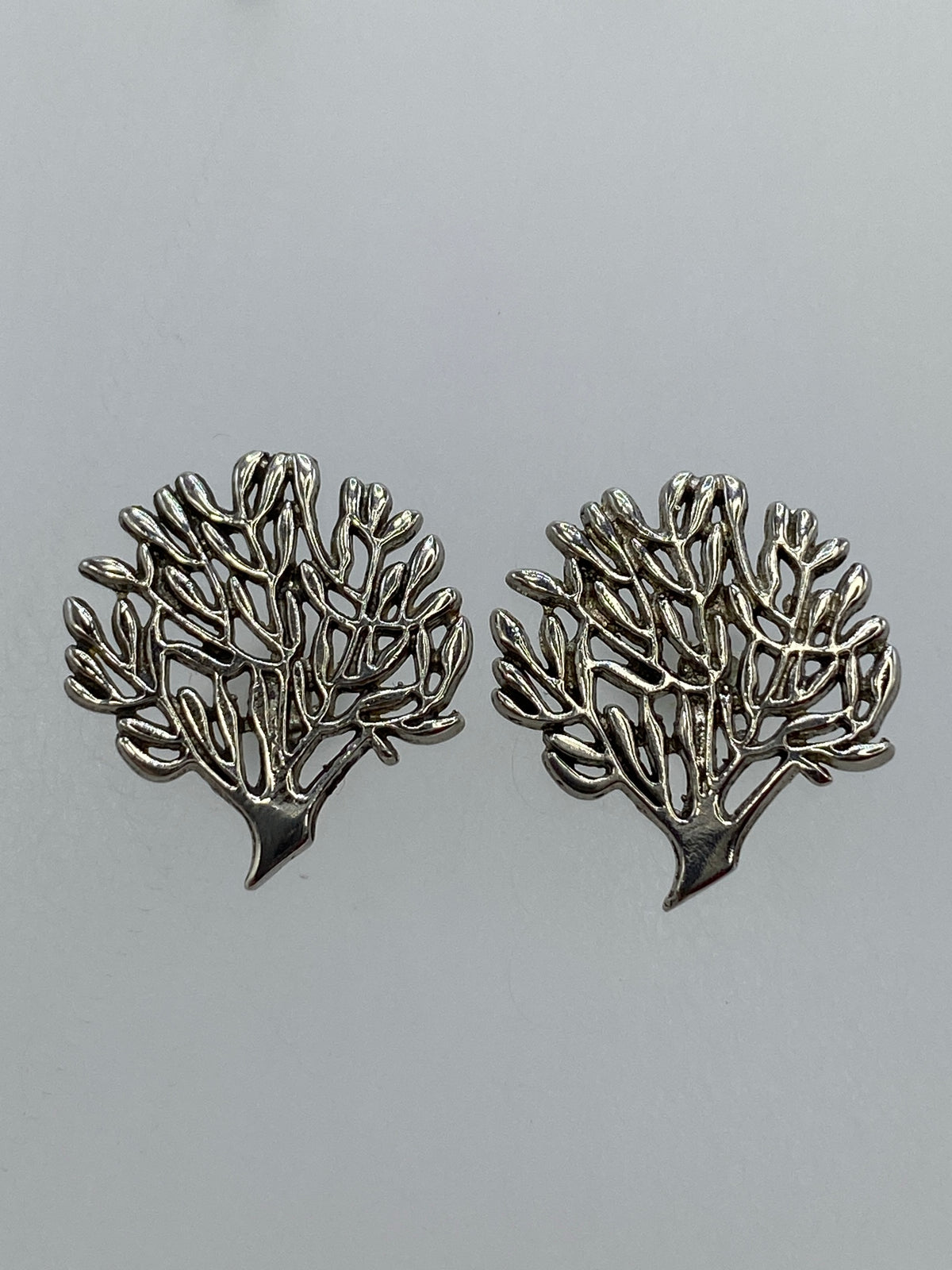 Par de aretes de plata en calado con diseño floral ramificado, sobre fondo gris