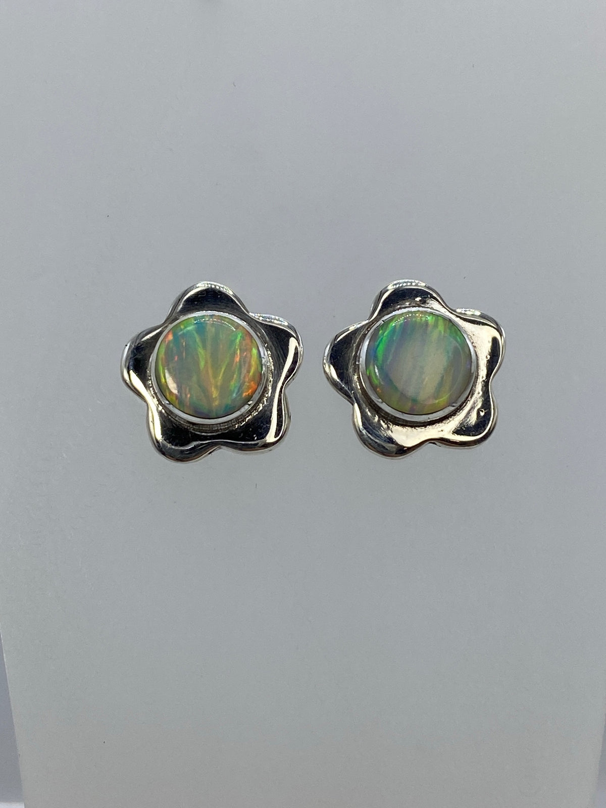 Detalle frontal de los aretes mostrando el juego de colores verde, oro y naranja del ópalo