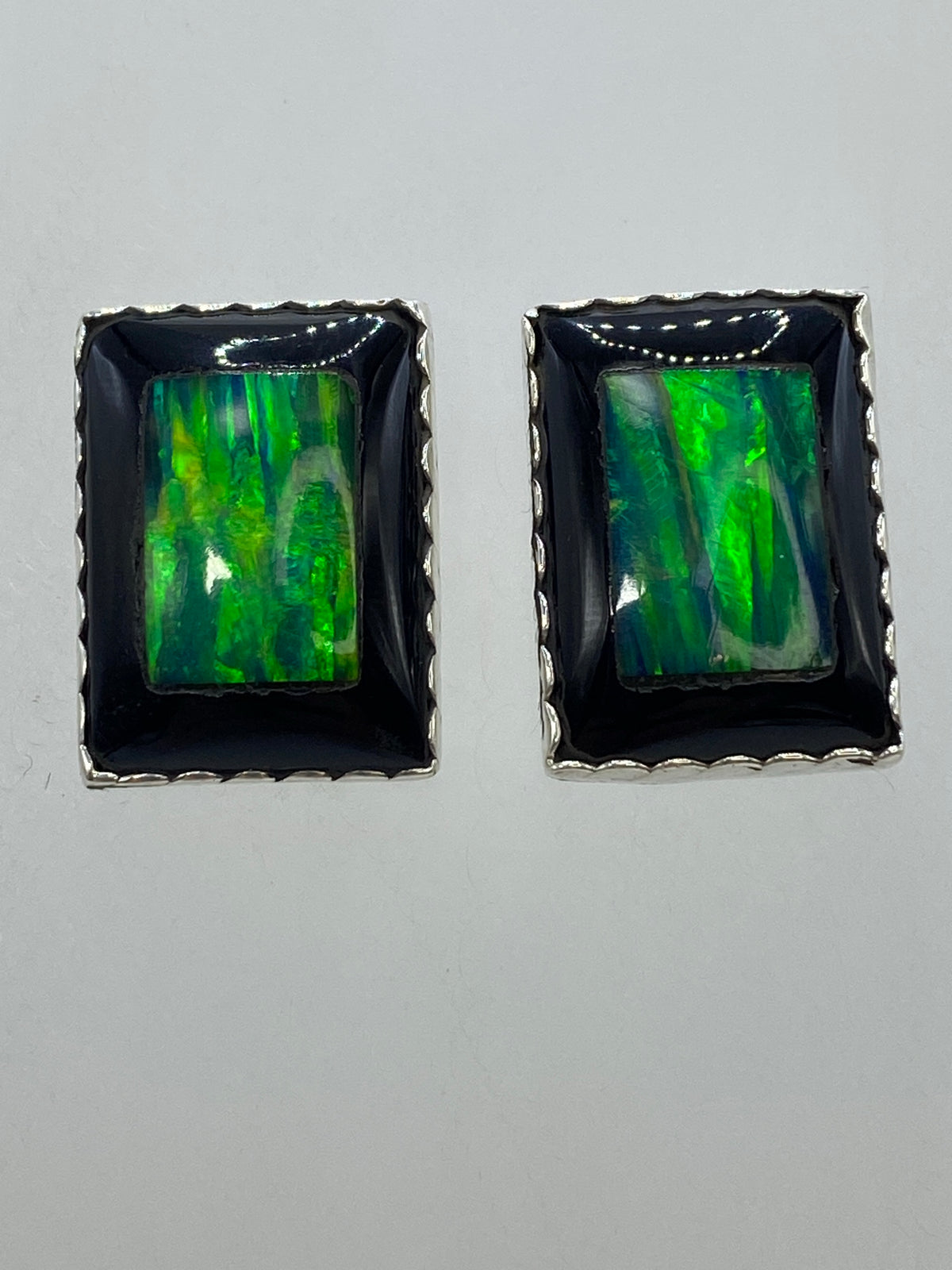 Par de aretes de plata 950 con ópalo de fuego verde, vista frontal sobre fondo blanco