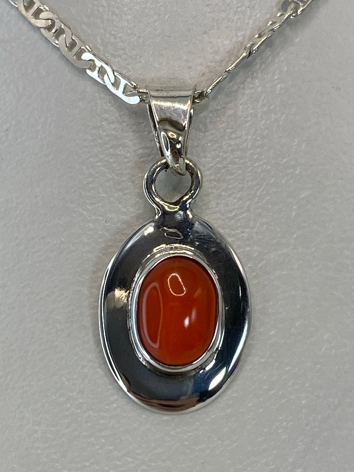 Dije de plata con piedra naranja en el pecho, suspendido de una cadena plateada