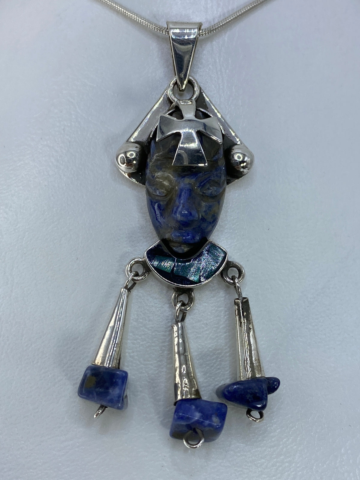 Dije de plata con cabeza azteca tallada y piedra azul engastada, colgando de cadena de plata