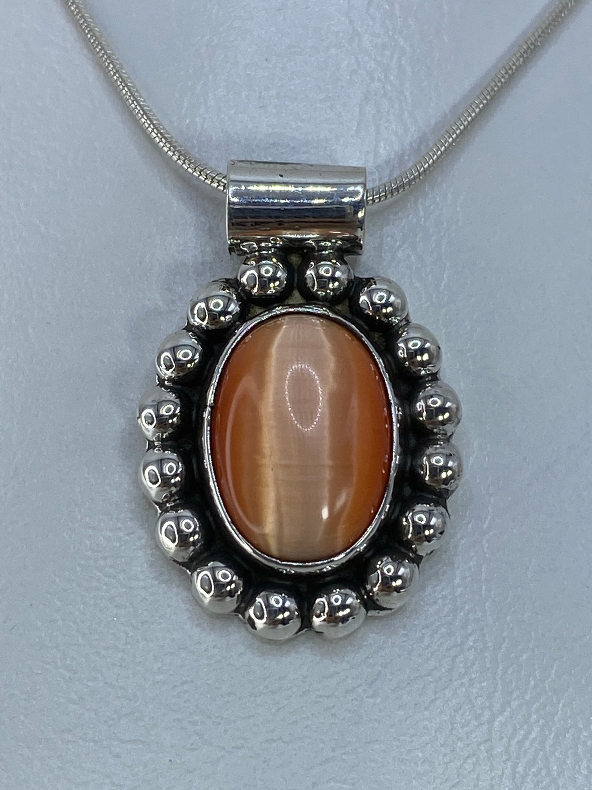 Dije de plata 925 con Ojo de Gato naranja, vista frontal mostrando el reflejo luminoso de la piedra