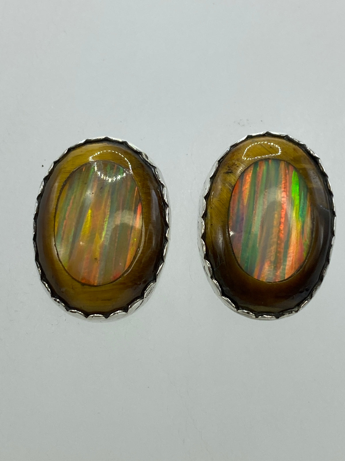Par de aretes de plata 950 con opalo de fuego multicolor y ojo de gato cafe, vistos de frente sobre fondo blanco
