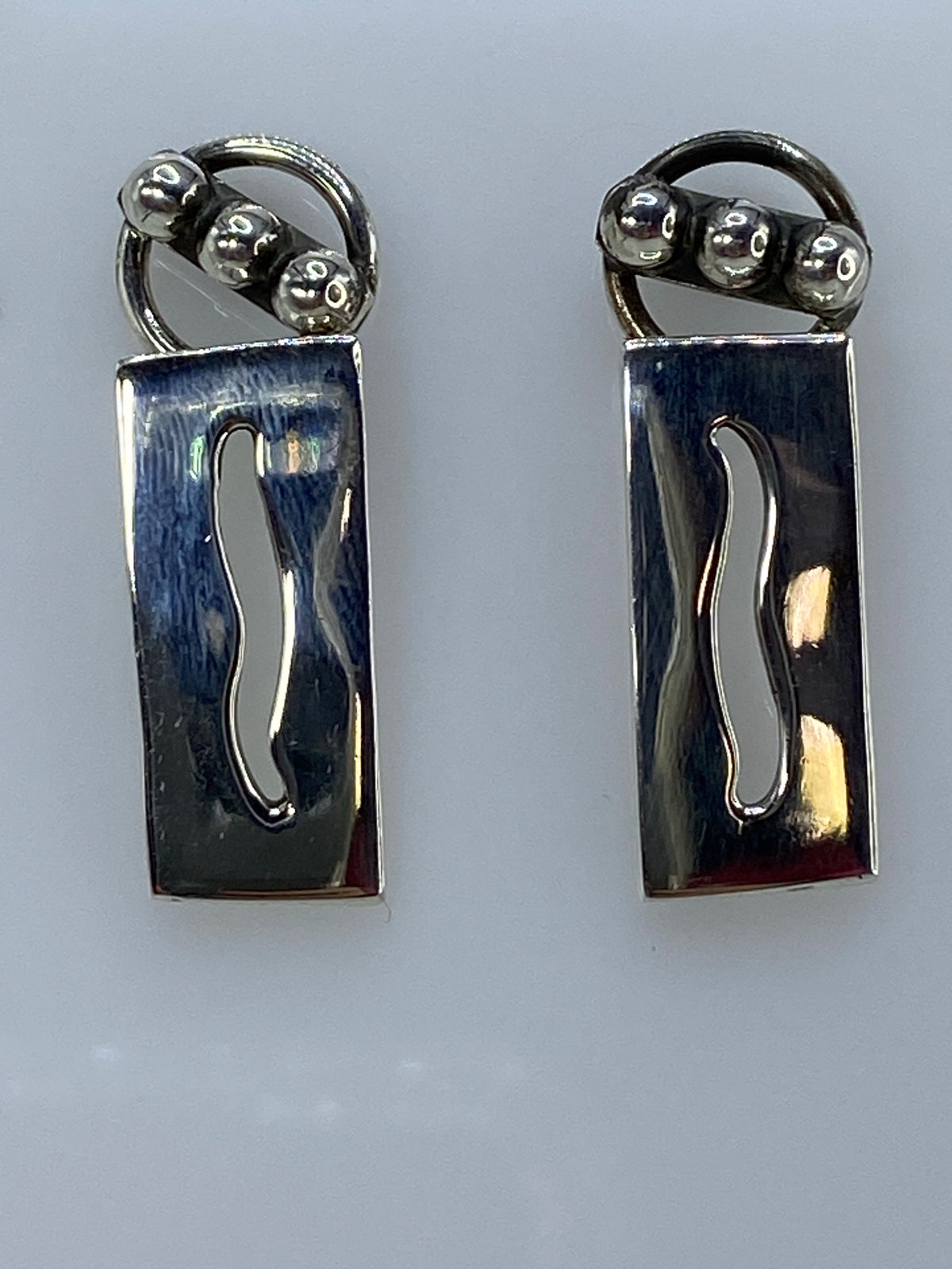 Par de aretes de plata cartoneado minimalista, rectangulares con curva, en color gris plateado