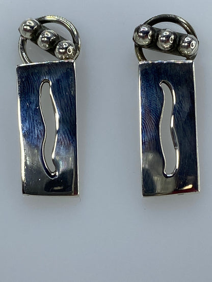 Aretes sobre fondo azul para escala, pesados en báscula mostrando 12.18 gramos totales