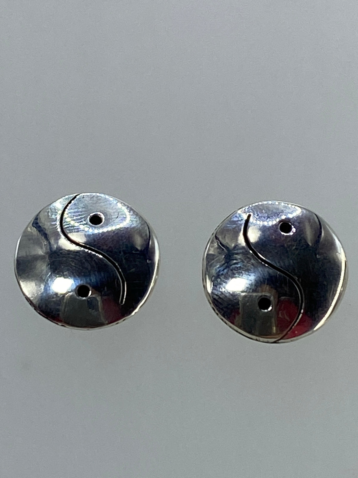 Aretes Yin Yang colocados sobre fondo azul para escala visual