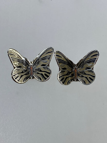 Vista frontal de los aretes de mariposa mostrando el relieve del cuerpo y las líneas de las alas