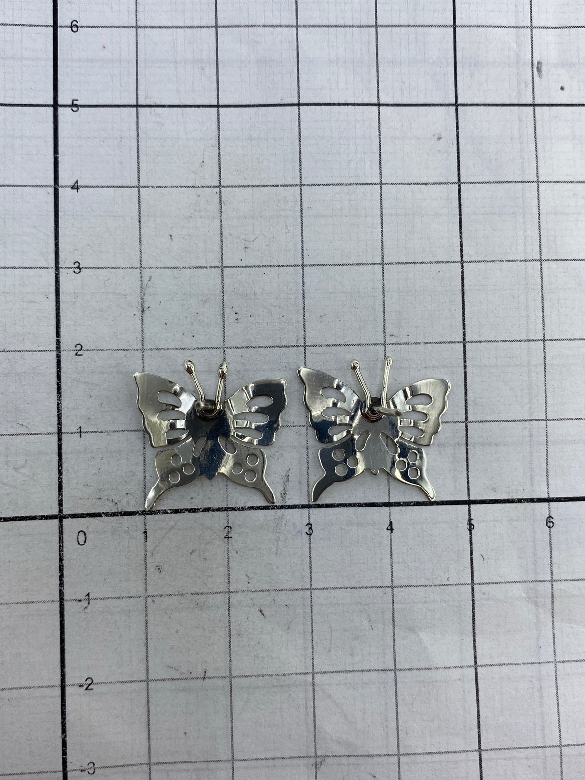 Aretes mariposa de plata sobre fondo blanco, tamaño y acabado real
