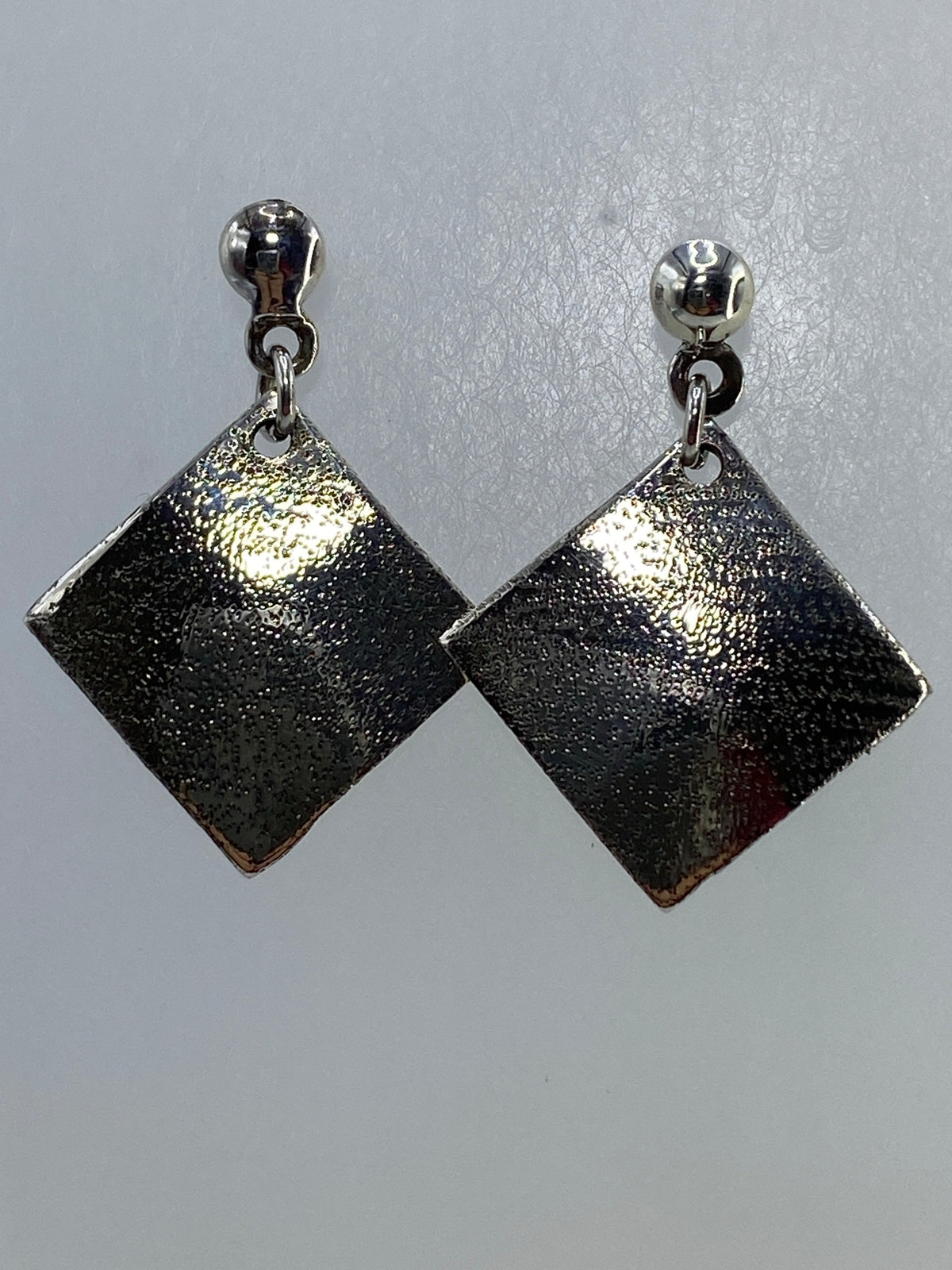 Par de aretes cuadrados de plata repujada, colgando de aros plateados
