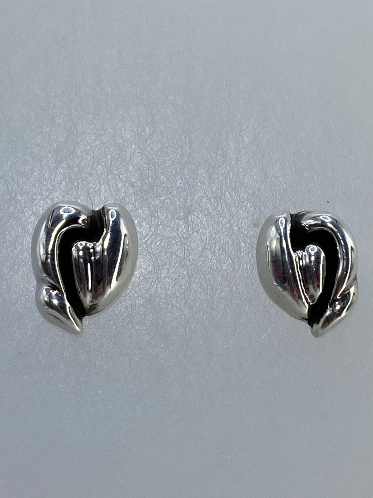 Aretes corazón de plata pura sobre fondo neutro con luz reflejada