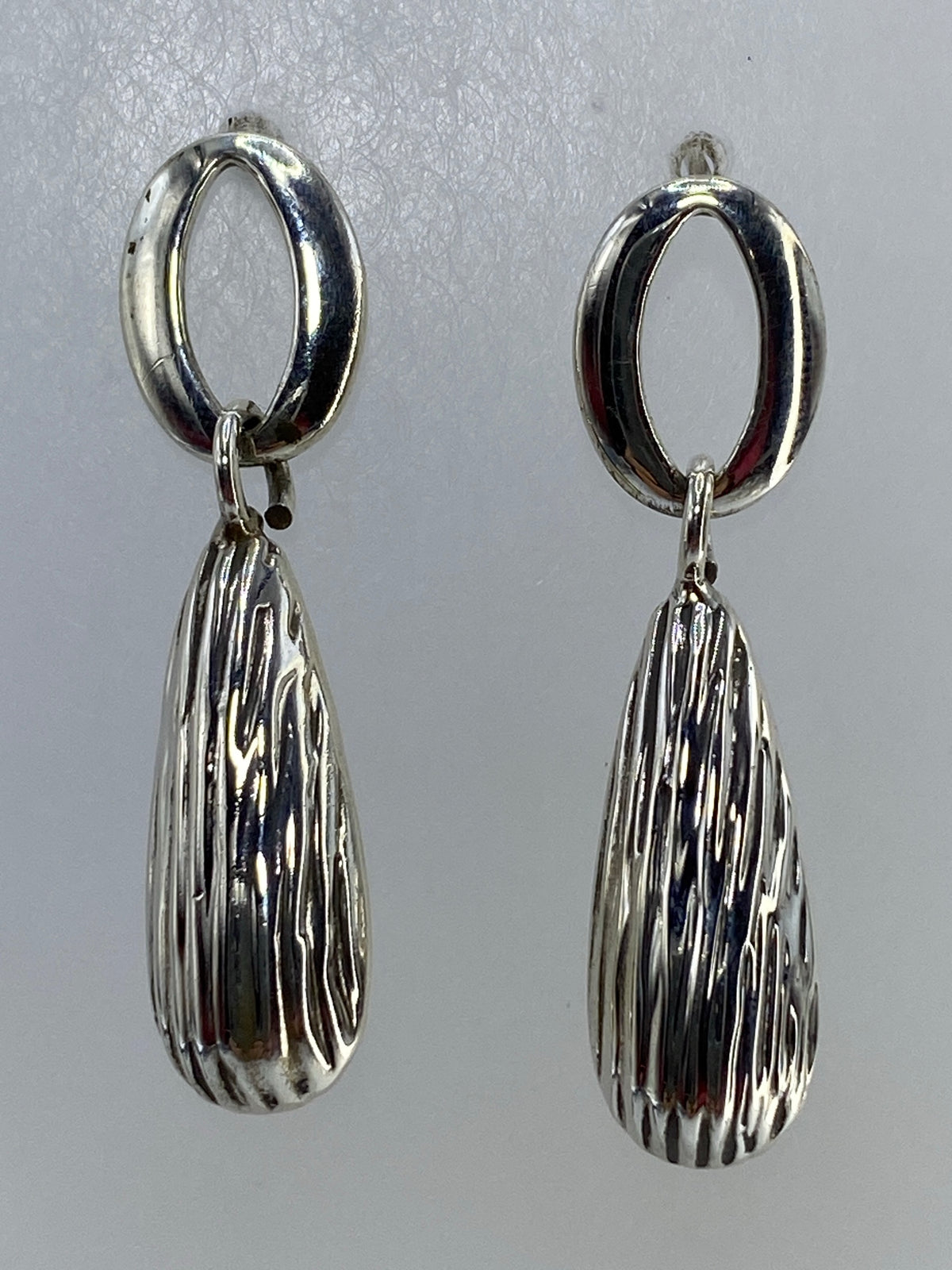Par de aretes de plata cartoneado con forma de gota colgando en primer plano