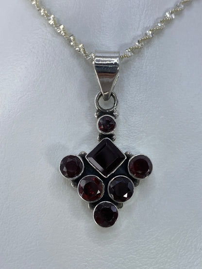 Dije de plata con circonia morada en forma de diamante central rodeado de círculos, colgando de cadena plateada