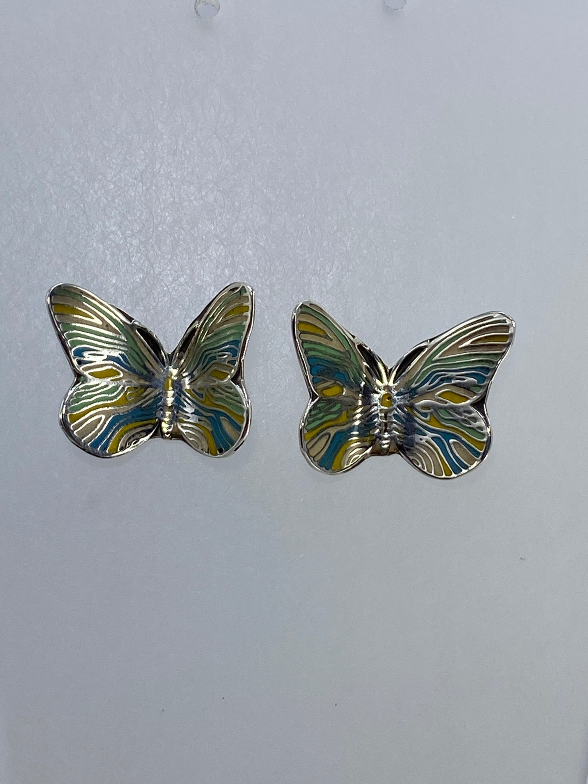 Vista frontal de arete de mariposa de plata con volumen 3D y patina