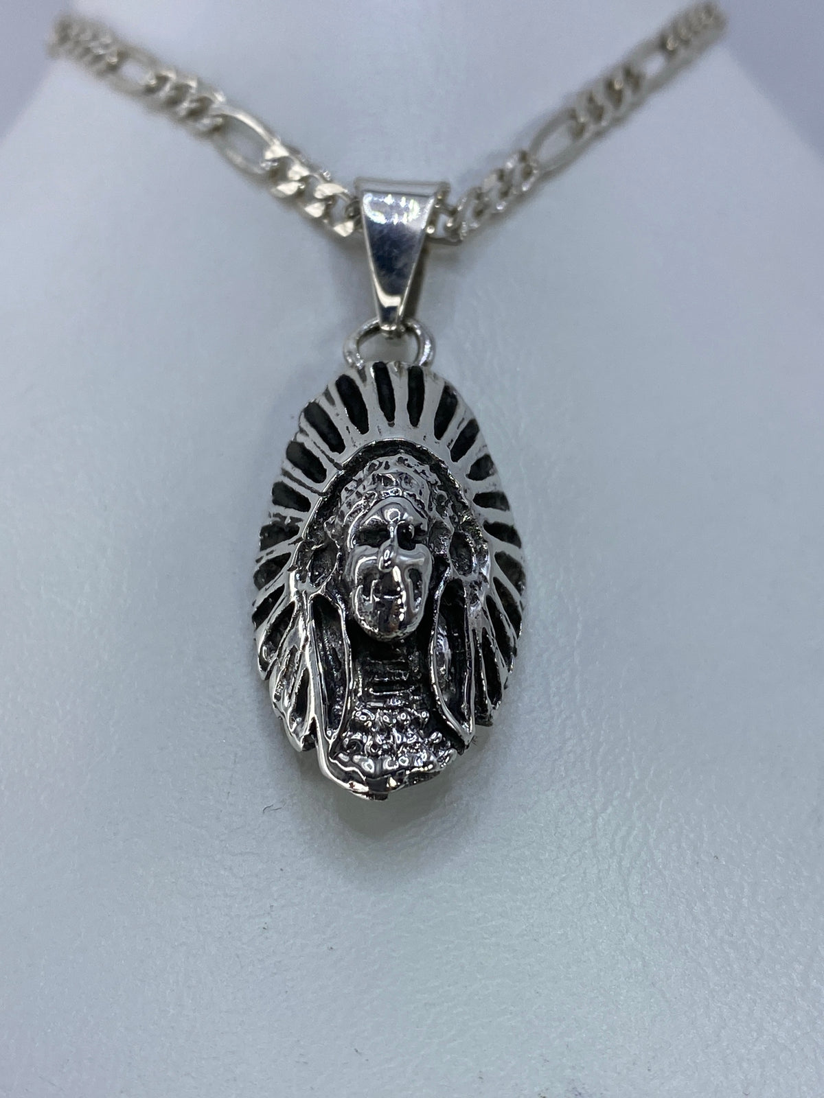 Detalle frontal del dije mostrando el rostro del guerrero indígena y los detalles del tocado