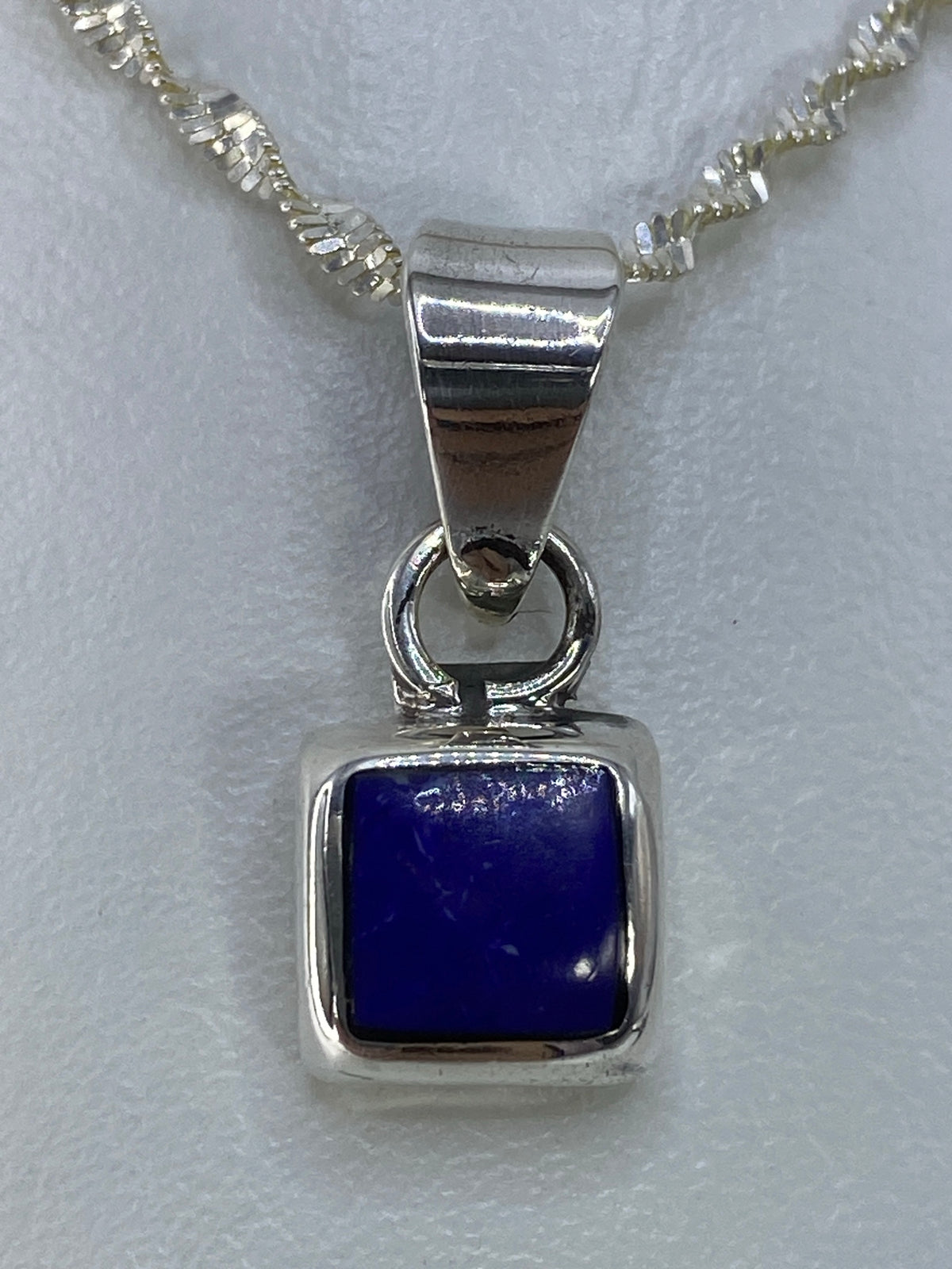 Dije cuadrado de plata con piedra azul engastada, colgando de cadena