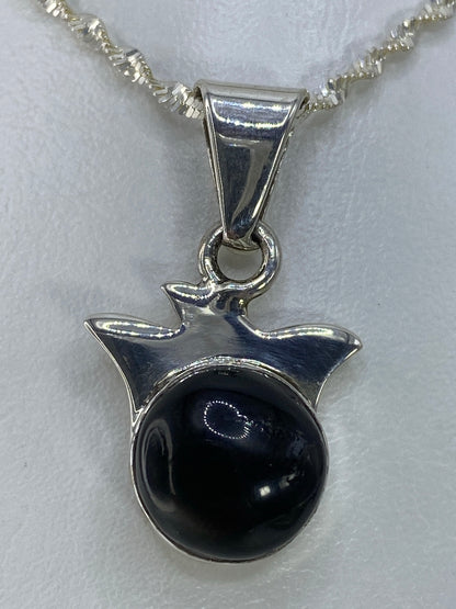 Dije de plata con piedra negra engastada, colgando de cadena plateada