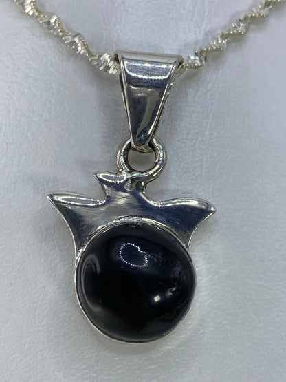 Detalle frontal del dije mostrando la piedra negra pulida y el engaste en plata 925