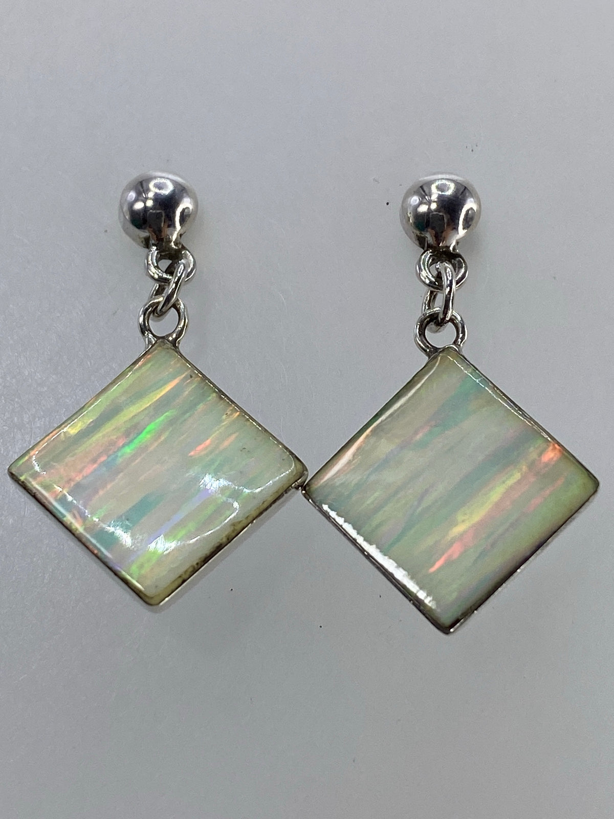 Los dos aretes de plata 925 con incrustación de ópalo sobre fondo blanco con escala de medida