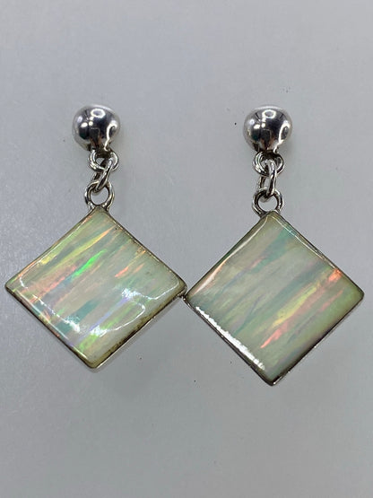 Los dos aretes de plata 925 con incrustación de ópalo sobre fondo blanco con escala de medida