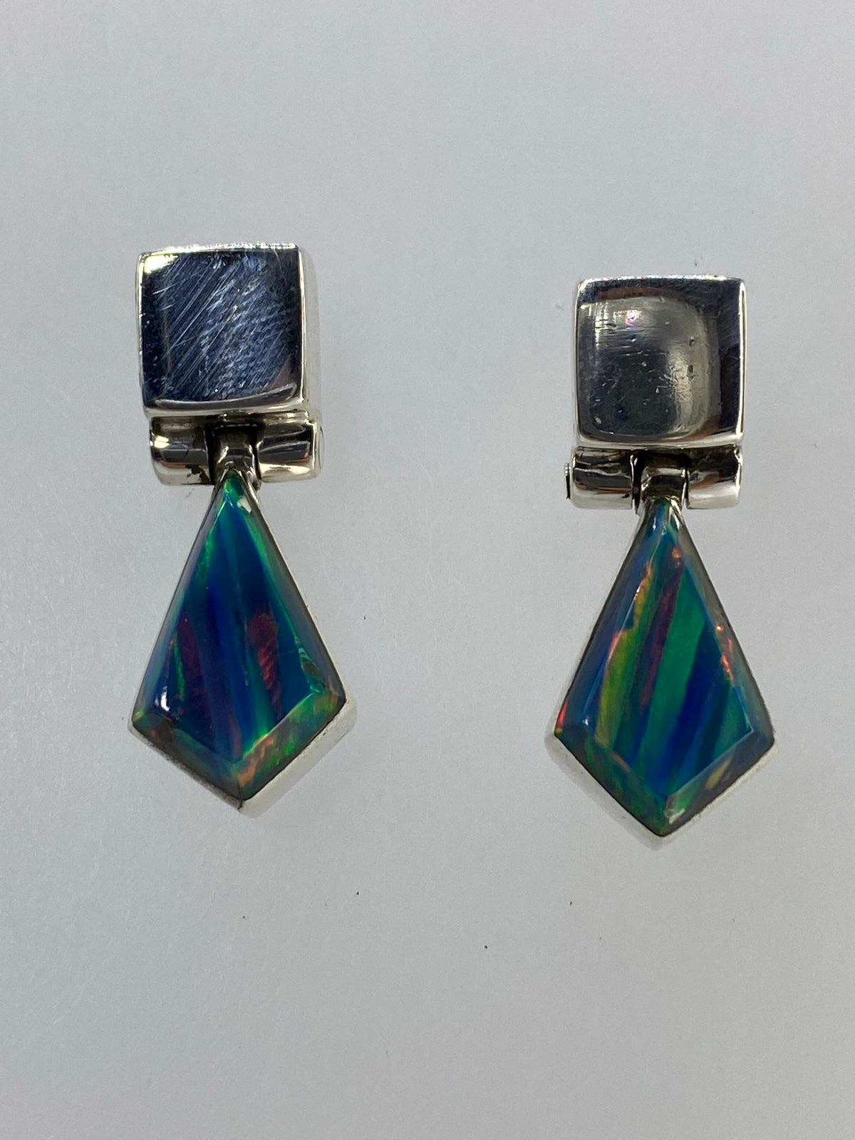 Aretes de plata 950 con ópalo de fuego multicolor facetado, par simétrico sobre fondo neutro