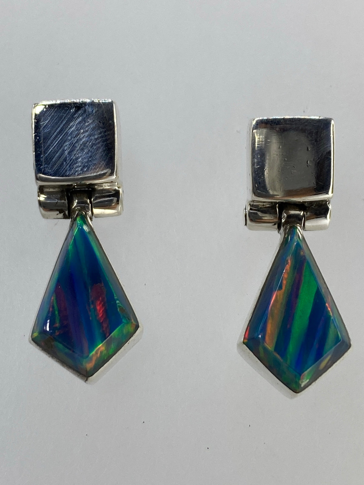 Aretes de ópalo multicolor junto a regla métrica para escala, demostrando el tamaño de la gota
