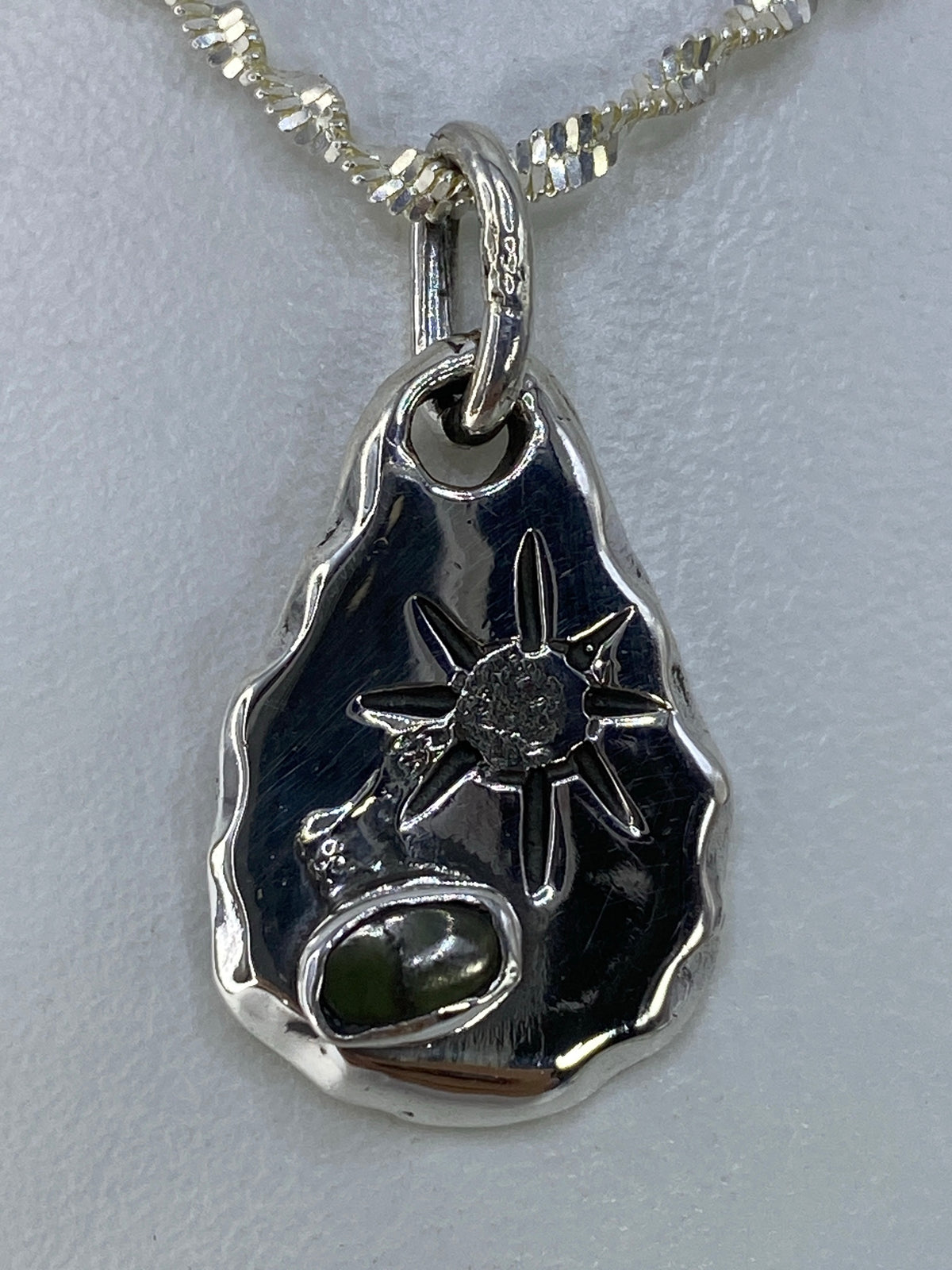 Dije de plata en forma de gota con piedra verde engastada, vista frontal sobre cadena